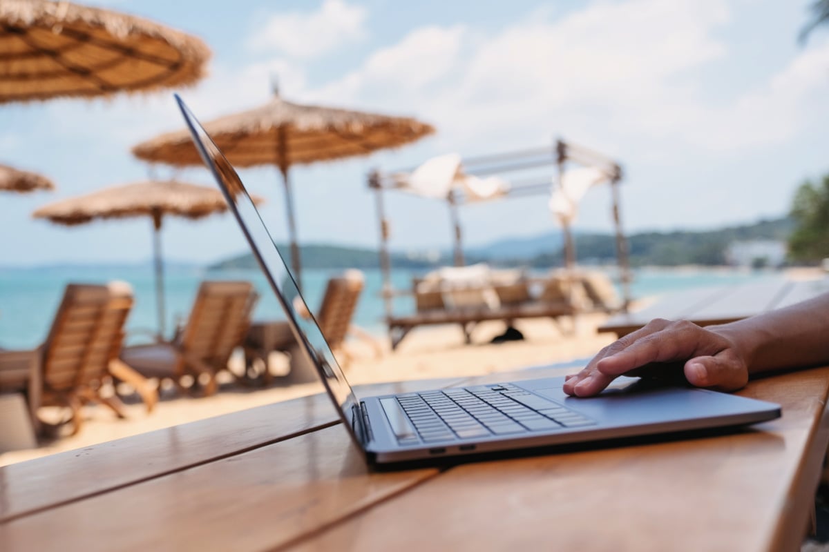 Digital nomad working from laptop outdoors at beach