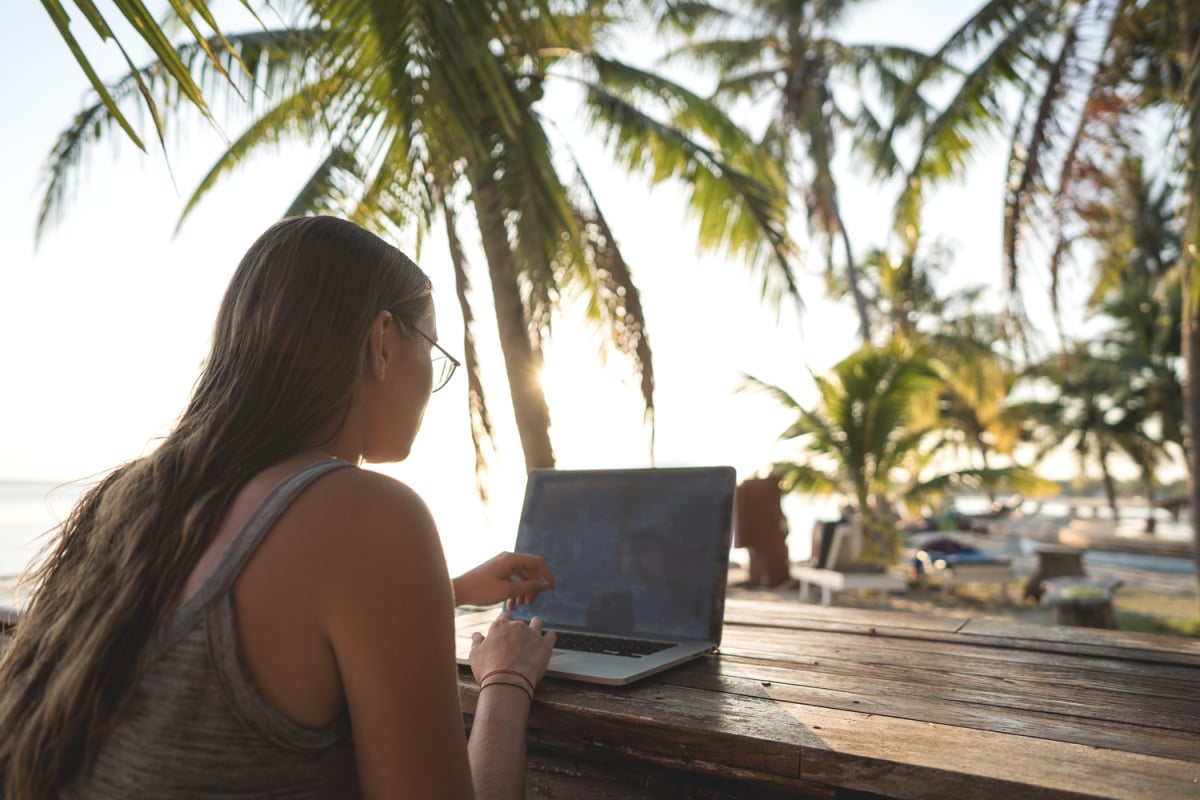 Digital nomad working on laptop under palm trees
