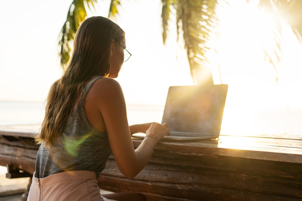 Digital nomad with laptop under palm tree